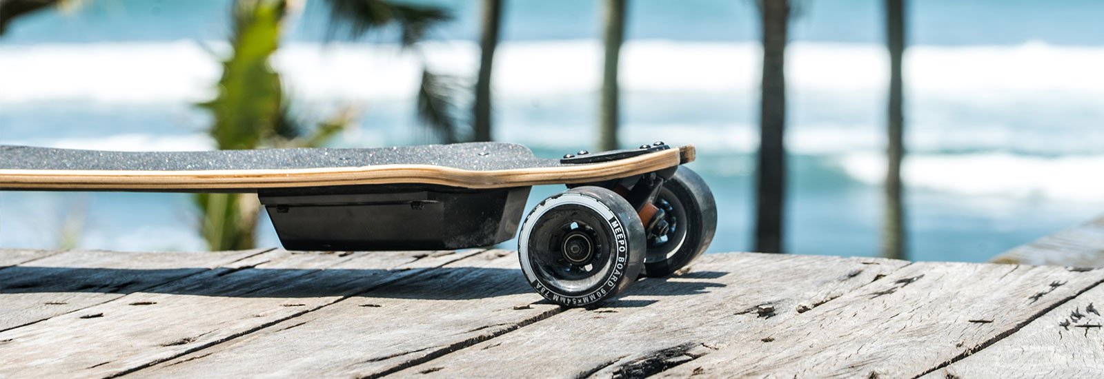 An electric skateboard on a wooden surface with a blurred beach background.