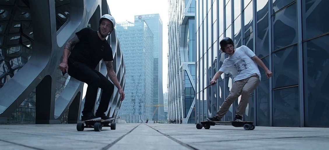 Two men wearing helmets riding electric skateboards on the street