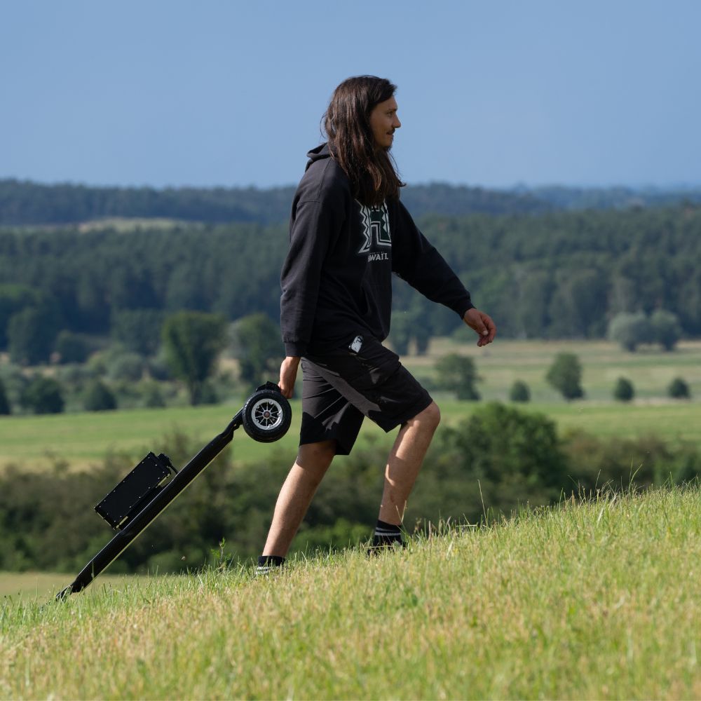Rider carrying Meepo electric skateboard on a grassy hill