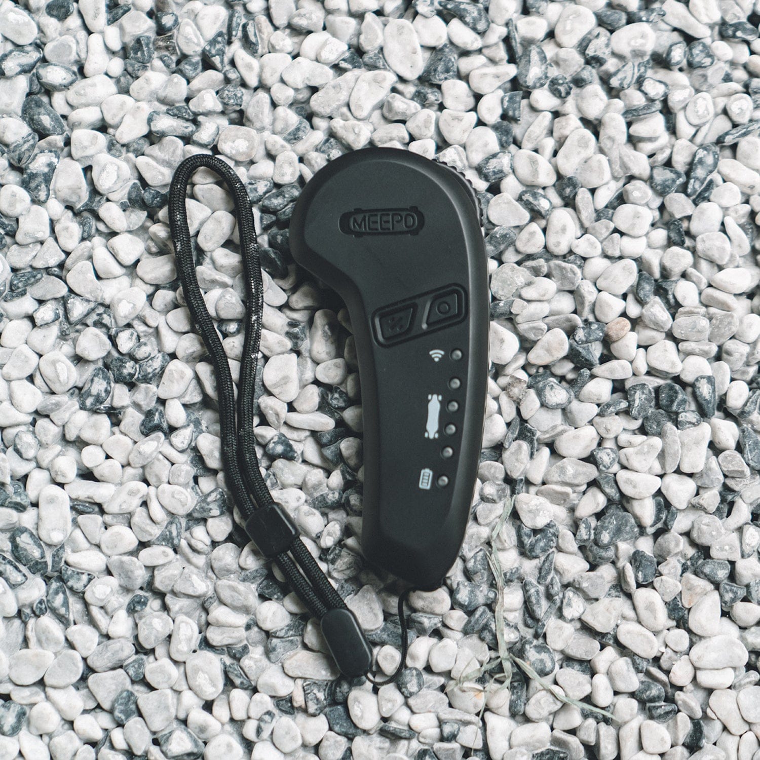 Meepo M5 skateboard remote with buttons and wrist strap on pebble surface