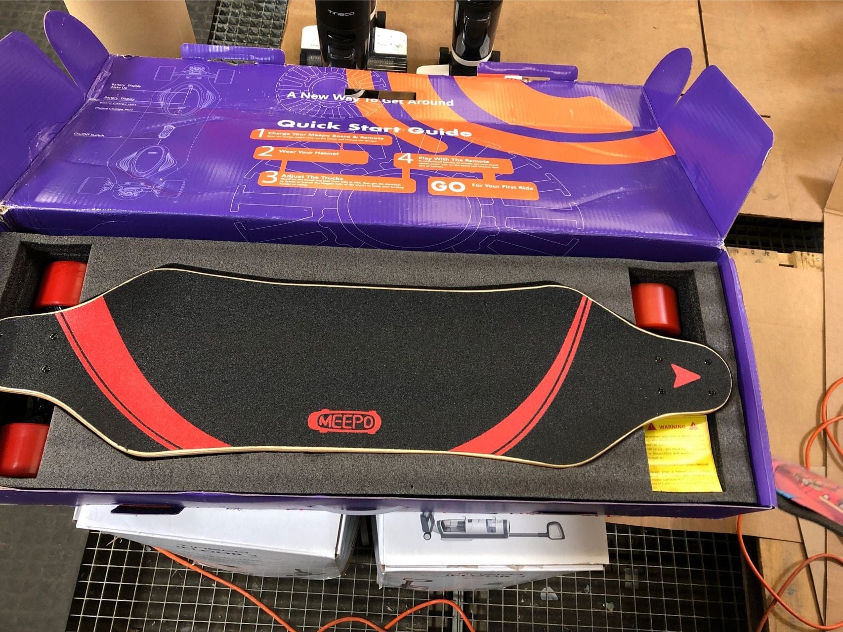 Meepo refurbished electric skateboard with black deck and red wheels in open packaging.